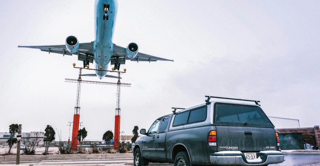 A striking image capturing an airplane landing closely over a parked truck on a tarmac.